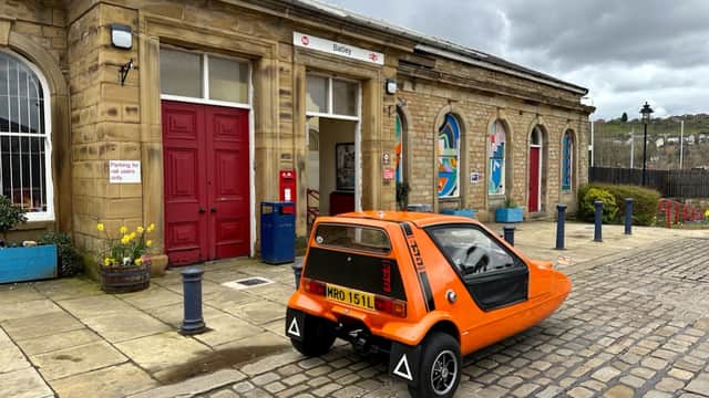 Batley Station features a historic stone building, an orange car parked outside, and colorful planters along the walkway.