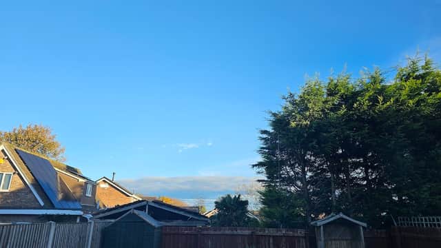 Clear blue sky over residential buildings and greenery, with a wooden fence and garden features in the foreground.