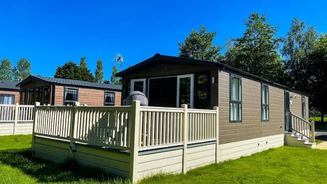 A modern lodge with a deck, surrounded by green grass and trees, under a clear blue sky in Allerthorpe, Yorkshire.