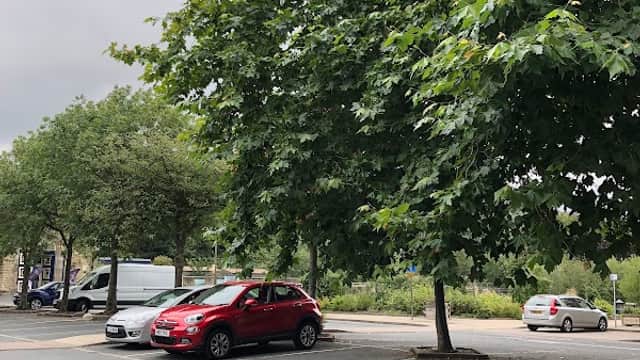 Bramsche Square car park with several trees and parked cars under a cloudy sky.