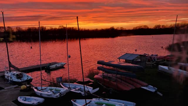 Sailboats and kayaks on the shore at sunset, reflecting vibrant orange and pink hues over the calm water.
