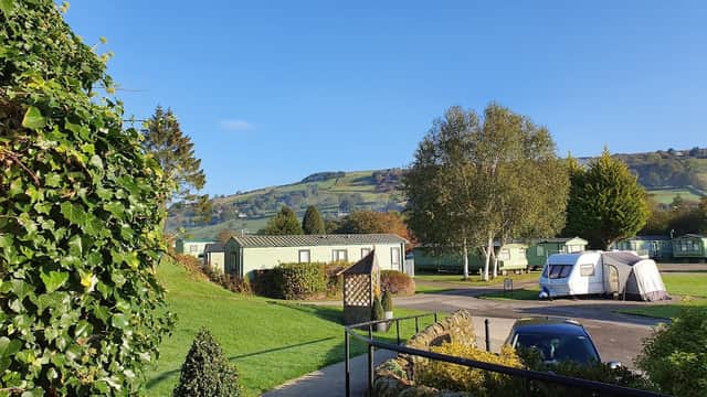 Caravans nestled among greenery with rolling hills in the background under a clear blue sky at Riverside Caravan Park.