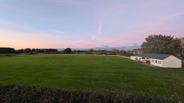 Cricket pitch with lush green grass, a white building, and a pastel sky at sunset in Hirst Courtney, Yorkshire.
