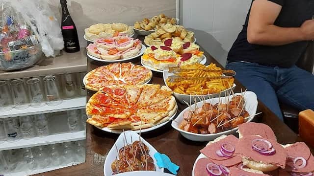 A table filled with various pub snacks, including pizzas, sandwiches, fries, and drinks, in a cozy pub setting.