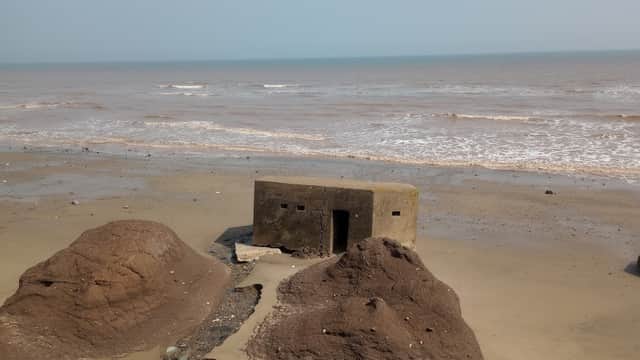 A weathered concrete structure on a sandy beach, with waves lapping at the shore and rocky formations nearby.
