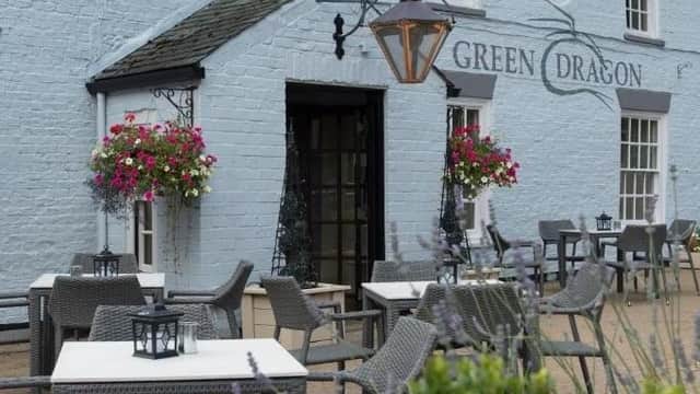 Light blue exterior of the Green Dragon bar, featuring hanging flower baskets, outdoor seating, and lanterns.