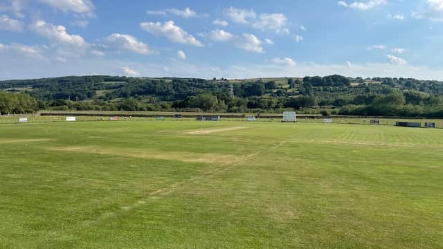 Lush green cricket pitch with a clear blue sky and rolling hills in the background at Airedale Cricket Club.