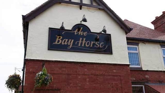 Sign for "The Bay Horse" guest house with a decorative design, set against a red brick building in East Cowick, Yorkshire.