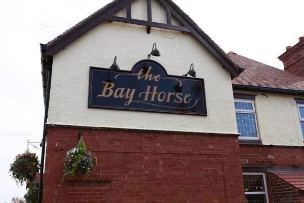 Sign for "The Bay Horse" guest house with a decorative design, set against a red brick building in East Cowick, Yorkshire.