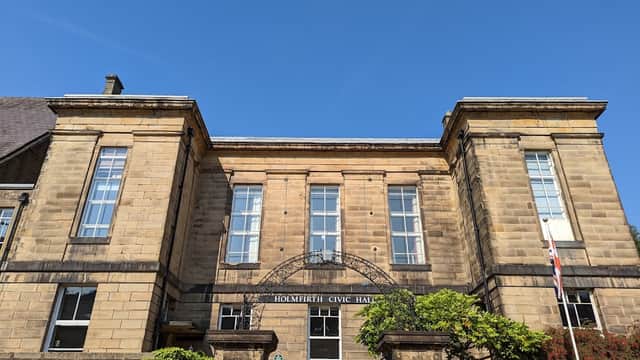 Historic stone building with large windows, greenery, and a flag, set against a clear blue sky.