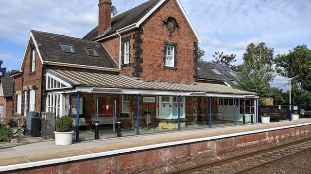 Brick building with large windows, covered platform, and train tracks under a blue sky at Poppleton Station Car Park.