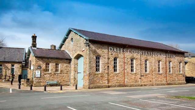 Historic stone building with large windows, sign reading "Dales Countryside Museum," and a person standing nearby.
