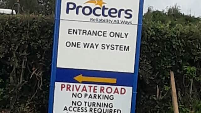 Procters Coaches sign with "Entrance Only," "One Way System," and "Private Road" instructions, surrounded by greenery.