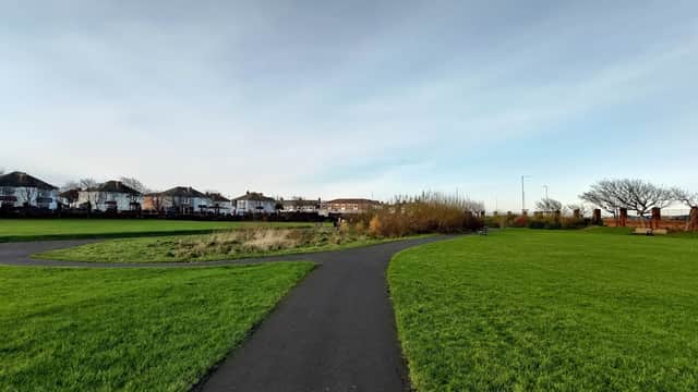 Path winding through a grassy area with houses in the background under a clear sky.