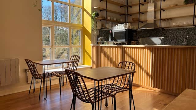 Bright café interior with wooden tables, woven chairs, and a coffee counter against a sunny window backdrop.