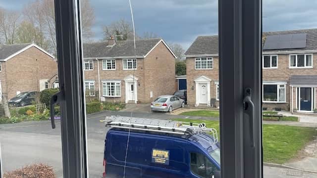 View through a window showing a blue van parked in front of houses under a cloudy sky in North Frodingham.
