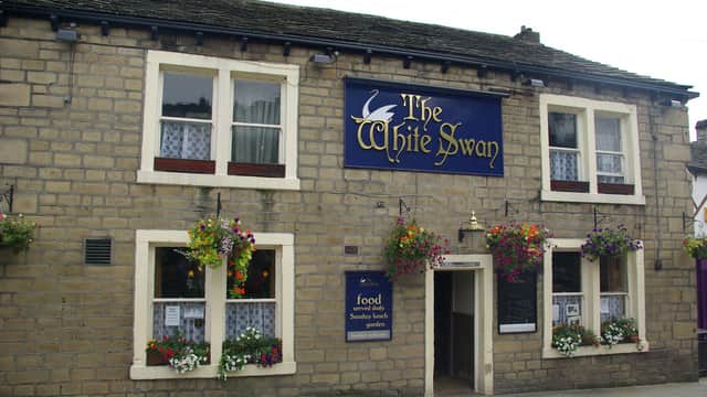 Stone building with a blue sign reading "The White Swan," adorned with colorful flower baskets and white-framed windows.