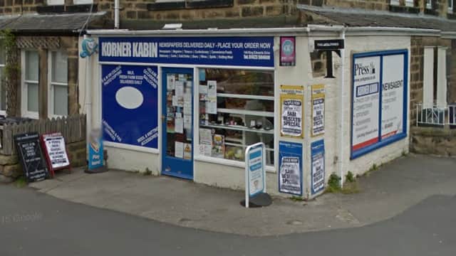 Local off-licence with a blue sign, window displays, and a sandwich board outside, set in a stone building.