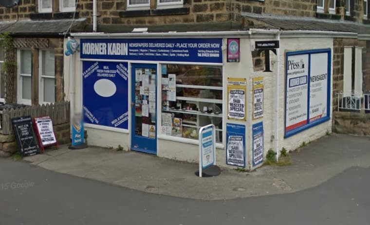 Local off-licence with a blue sign, window displays, and a sandwich board outside, set in a stone building.