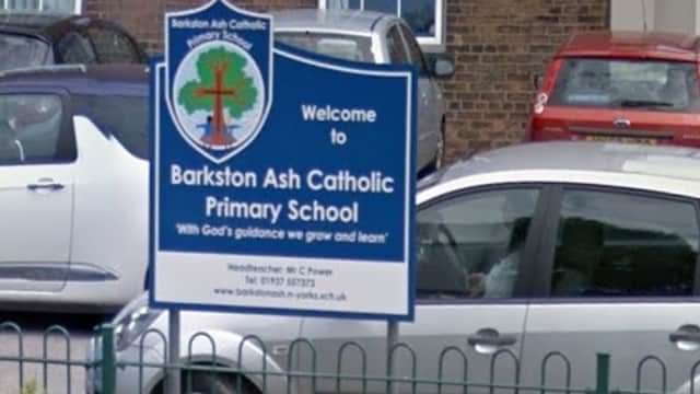 Welcome sign for Barkston Ash Catholic Primary School with colorful flowers and parked cars in front.
