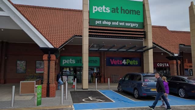 Pet shop entrance with "pets at home" and "Vets4Pets" signs, parking spaces, and shoppers approaching the store.