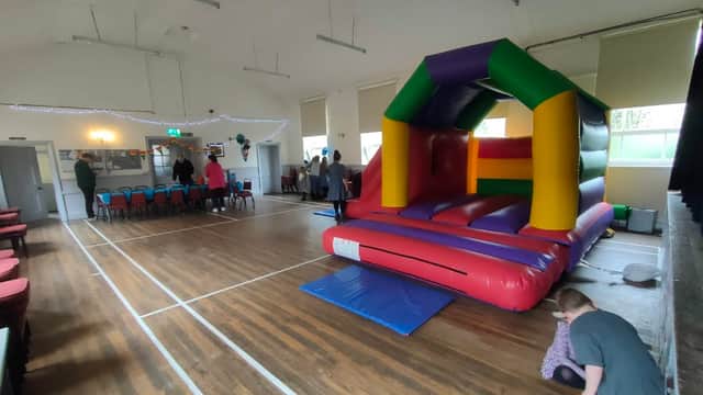 Colorful bouncy castle in a hall with wooden floors and chairs arranged in the background, people interacting nearby.