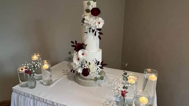 Elegant three-tier cake adorned with flowers and greenery, surrounded by lit candles on a draped table.