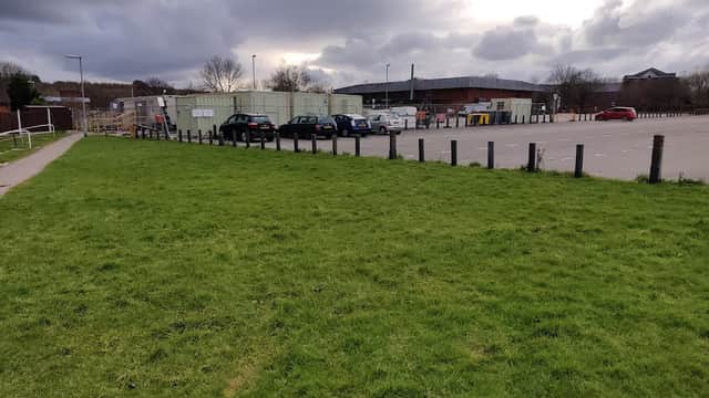 Grassy area in foreground with a car park in the background, featuring parked cars and overcast skies.
