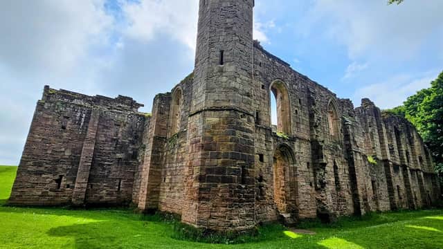 Ruins of Spofforth Castle featuring stone walls, arched windows, and a tower, surrounded by lush green grass.