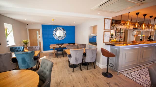 Stylish bar interior with blue accent wall, wooden tables, plush chairs, and a well-stocked bar area.