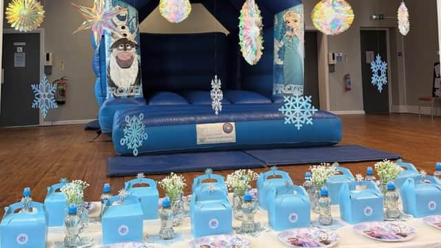 A blue bouncy castle with Frozen characters, decorated tables with blue party boxes and floral arrangements.