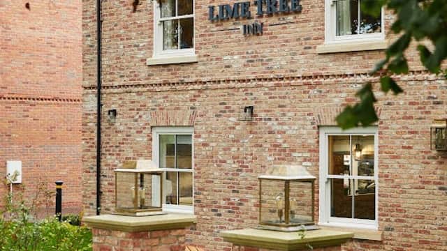 Brick building with "The Lime Tree Inn" sign, surrounded by greenery and a pathway leading to the entrance.