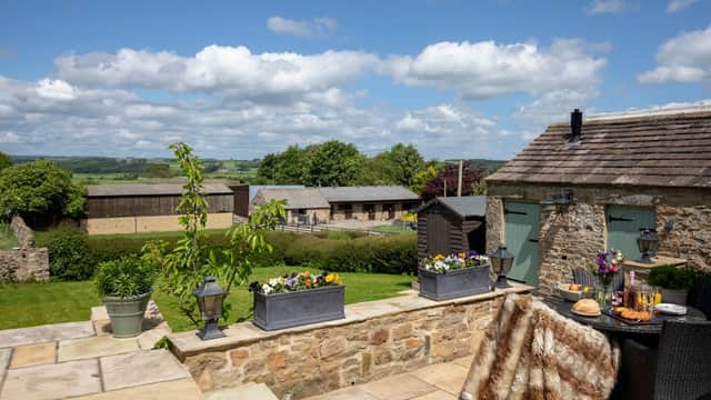 Scenic view of Manor House Cottages with stone walls, lush greenery, and flower planters under a bright blue sky.