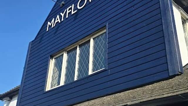 Blue wooden exterior of The Mayflower pub, featuring a prominent sign and diamond-patterned windows against a clear sky.