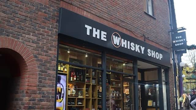 Brick building with large windows displaying various whisky bottles and a sign reading "The Whisky Shop."