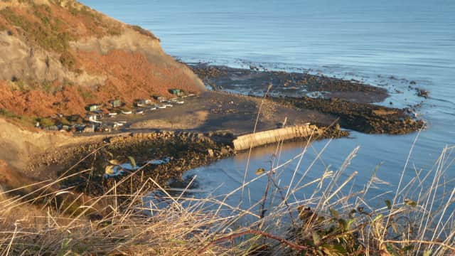 Coastal view of Hinderwell with rocky shoreline, calm sea, and distant cottages nestled among the cliffs.