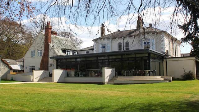 Modern glass extension of YHA York Hostel with a grassy area and trees in the background under a blue sky.