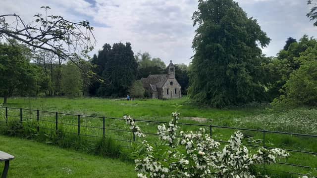 Historic stone church nestled among lush greenery and trees, surrounded by a meadow and blooming white flowers.