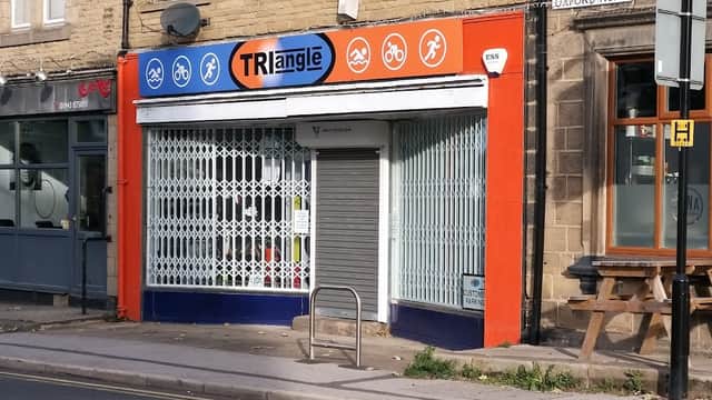 Bicycle shop with a colorful sign featuring bike icons, a closed shutter, and a bike rack outside on a street.