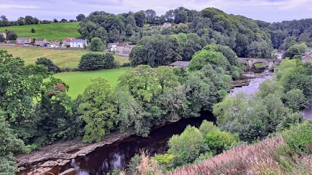 Lush green hills with trees, a river winding through, and quaint houses in Hudswell, North Yorkshire.