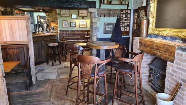Cozy pub interior with wooden bar stools, a rustic bar, stone walls, and a fireplace, creating a warm atmosphere.