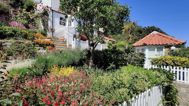 Lush garden with colorful flowers, a white picket fence, and a charming gazebo under a clear blue sky.