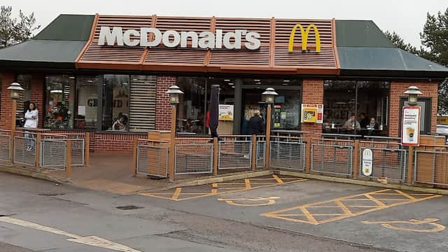 McDonald's restaurant exterior with large windows, outdoor seating, and a sign featuring the iconic golden arches.