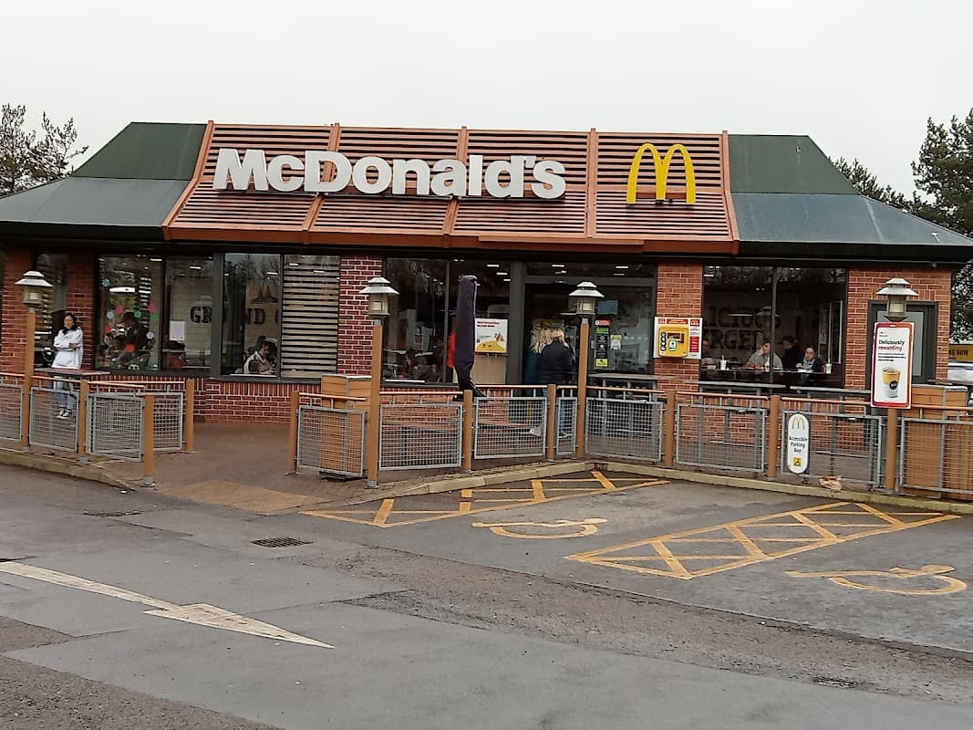 McDonald's restaurant exterior with large windows, outdoor seating, and a sign featuring the iconic golden arches.