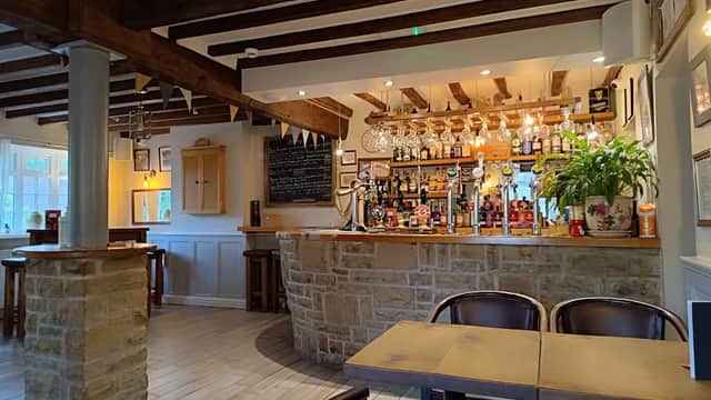 Cozy bar interior with wooden beams, a stone counter, colorful bottles, and a welcoming atmosphere in Bagby, Yorkshire.