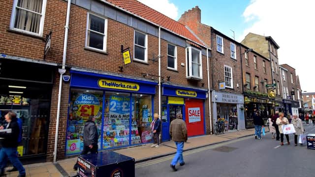 Colorful storefront of The Works bookshop, featuring books and toys, with pedestrians walking on a cobblestone street.
