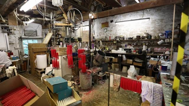 Workshop interior with red candles hanging, shelves filled with tools, and boxes scattered around a rustic space.
