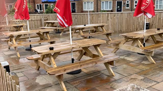 Outdoor seating area with wooden picnic tables, red umbrellas, and a stone patio at The Manor Inn in Fridaythorpe.