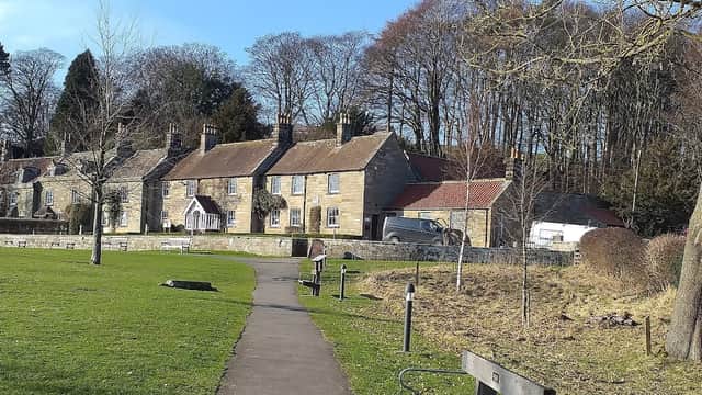 Pay & Display car park in Danby, featuring stone cottages, a pathway, benches, and surrounding trees.