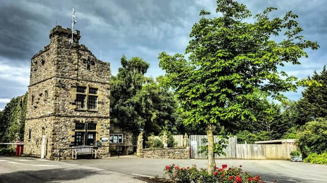 Stone building with a tower, surrounded by trees and flowers, under a cloudy sky at Akebar Park Golf Course.